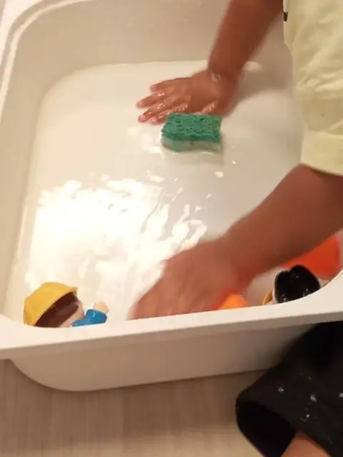 Mains d&rsquo;enfant jouant avec une &eacute;ponge et des figurines dans un bac d&rsquo;eau